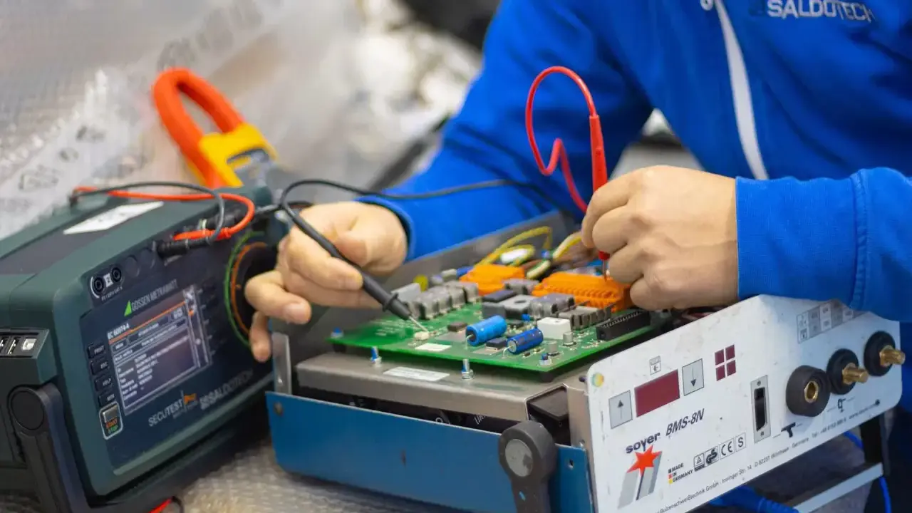 Tecnico effettua la riparazione di saldatrici, testando un circuito elettronico con strumenti di precisione.
