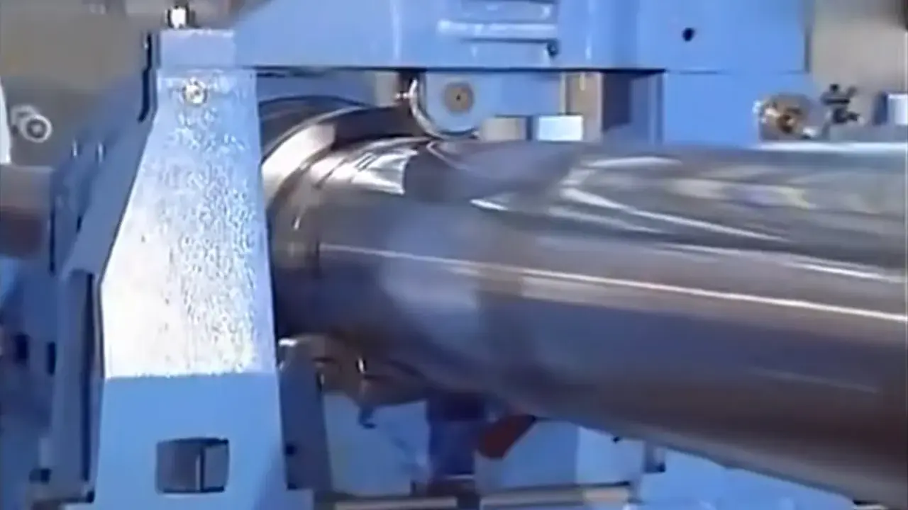 Macchinario industriale blu in azione, impegnato in una **foratura profonda** su un grande cilindro metallico lucido.