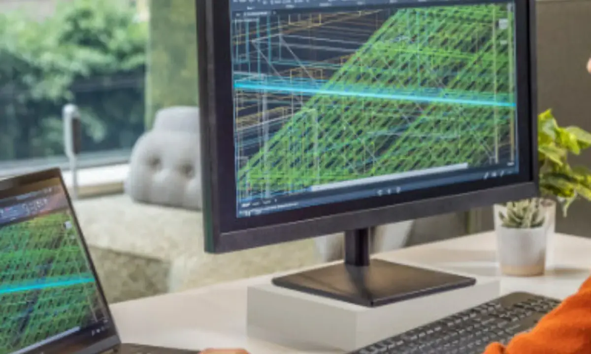 Un inventore lavora su un progetto complesso con AutoCAD, visualizzando modelli 3D su un monitor e un laptop.