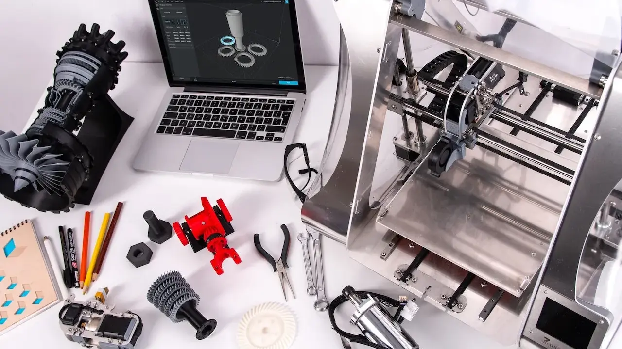 Un programmatore CNC progetta e stampa componenti complessi. Laptop con modello 3D, stampante 3D, parti meccaniche e attrezzi.