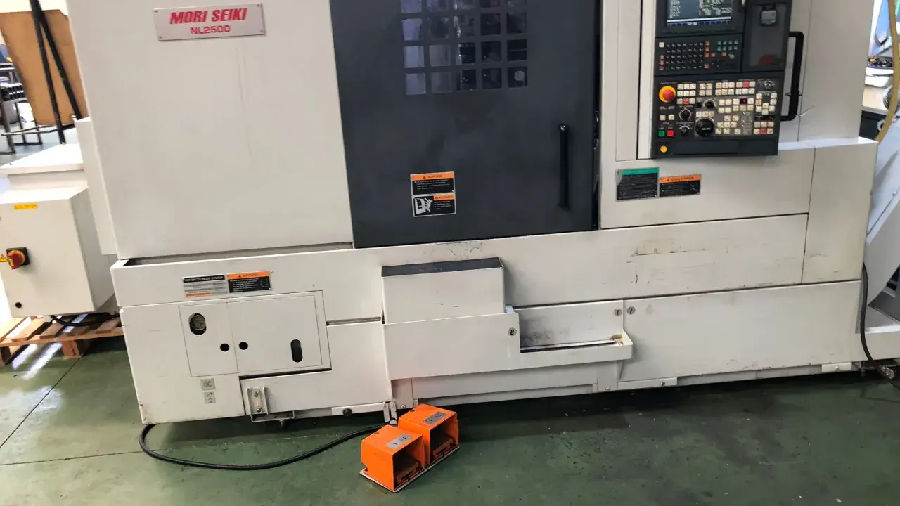 Tornio Mori Seiki NL2500 in officina, con pannello di controllo e pedali arancioni.