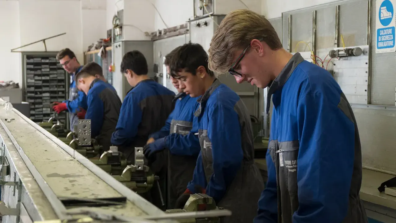 Giovani apprendisti in officina, concentrati sul loro lavoro. L'operatore meccanico cosa fa? Impara a usare strumenti e macchinari per creare e riparare componenti.