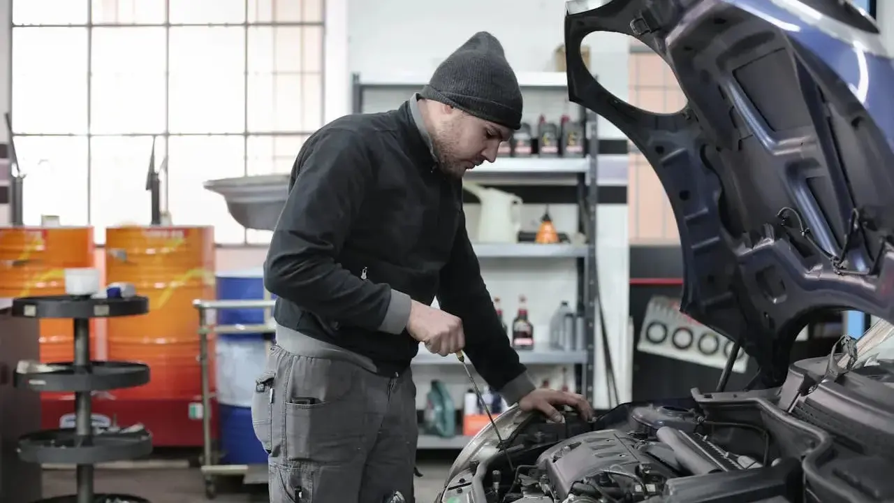 Giovane apprendista meccanico al lavoro, mentre controlla il motore di un'auto. Chissà quanto guadagna un apprendista meccanico con questa dedizione.