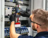 Tecnico con guanti neri lavora su un quadro elettrico, con un cacciavite su un componente. Il suo lavoro con il plc è fondamentale per l'automazione.