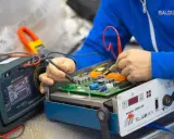 Tecnico effettua la riparazione di saldatrici, testando un circuito elettronico con strumenti di precisione.