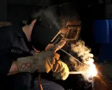 Saldatore con maschera e guanti, intento a lavorare. La scena evoca una tabella amperaggio saldatura elettrodo, con scintille e fumo.
