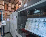 Schermata di un sistema di controllo plc in un magazzino automatizzato, con scaffali carichi di merce sullo sfondo.