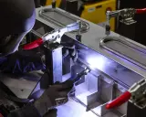 Saldatore esperto esegue saldatura di alluminio su una struttura metallica complessa, illuminata da un bagliore intenso.