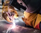 Saldatura tubi con guanti protettivi e maschera. Scintille e fumo illuminano il metallo.