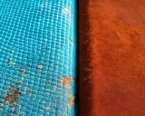 Dettaglio di un test di **salt spray** su due materiali: uno blu con macchie di corrosione, l'altro arancione.