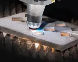 Macchina da taglio laser che crea forme precise su una lastra metallica. Il fascio luminoso e le scintille mostrano il **taglio termico**, un processo industriale avanzato.
