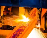 Un metallo incandescente subisce un trattamento termico, con scintille luminose che volano via.