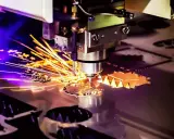 Macchina per **taglio laser** in azione, con scintille dorate che volano mentre crea forme precise su un foglio di metallo.