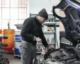 Giovane apprendista meccanico al lavoro, mentre controlla il motore di un'auto. Chissà quanto guadagna un apprendista meccanico con questa dedizione.