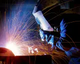 Un saldatore con maschera protettiva esegue lavori di saldatura, creando una pioggia di scintille luminose in un'officina buia.