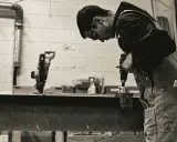 Giovane operatore CNC senza esperienza impara a usare un trapano, concentrato sul lavoro.