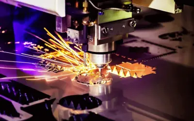 Macchina per **taglio laser** in azione, con scintille dorate che volano mentre crea forme precise su un foglio di metallo.