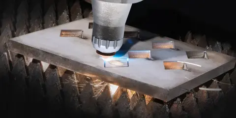 Macchina da taglio laser che crea forme precise su una lastra metallica. Il fascio luminoso e le scintille mostrano il **taglio termico**, un processo industriale avanzato.