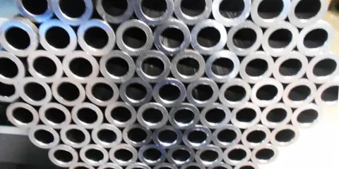 Un mucchio di tubi in acciaio al carbonio, con la sigla visibile su alcuni di essi, pronti per essere utilizzati.