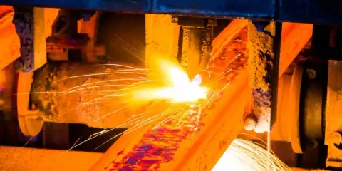 Un metallo incandescente subisce un trattamento termico, con scintille luminose che volano via.