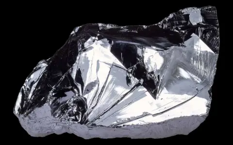 Frammento lucido di silicio puro, metallico, con sfaccettature che riflettono la luce. Il suo elevato punto di fusione lo rende fondamentale nell'elettronica.