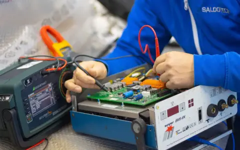 Tecnico effettua la riparazione di saldatrici, testando un circuito elettronico con strumenti di precisione.