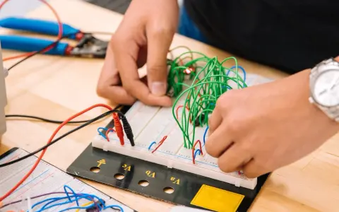 Mani che assemblano circuiti su breadboard, un'attività che fa riflettere su quanto guadagna un meccanico industriale.