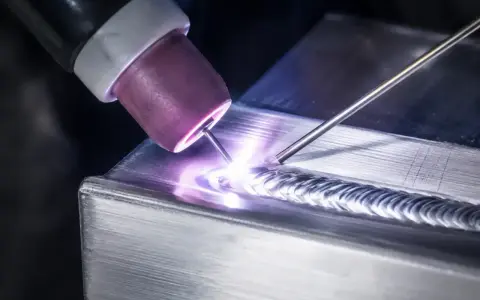 Saldatura magnesio con torcia TIG, creando un cordone preciso e luminoso su un pezzo metallico.