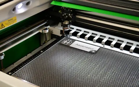 Macchina per taglio laser in azione, che realizza un cartello "Ascenseur" con simboli per bagni. Perfetta per progetti di taglio laser personalizzati.