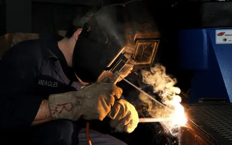 Saldatore con maschera e guanti, intento a lavorare. La scena evoca una tabella amperaggio saldatura elettrodo, con scintille e fumo.