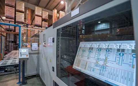 Schermata di un sistema di controllo plc in un magazzino automatizzato, con scaffali carichi di merce sullo sfondo.