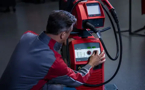 Operatore regola i parametri di saldatura su una macchina Fronius, ottimizzando l'apporto termico per un lavoro preciso.