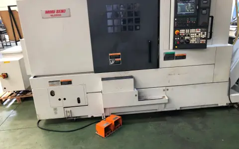 Tornio Mori Seiki NL2500 in officina, con pannello di controllo e pedali arancioni.