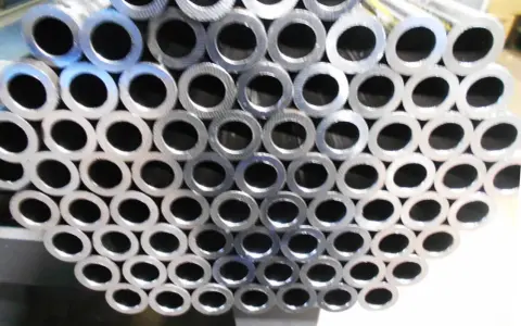 Un mucchio di tubi in acciaio al carbonio, con la sigla visibile su alcuni di essi, pronti per essere utilizzati.