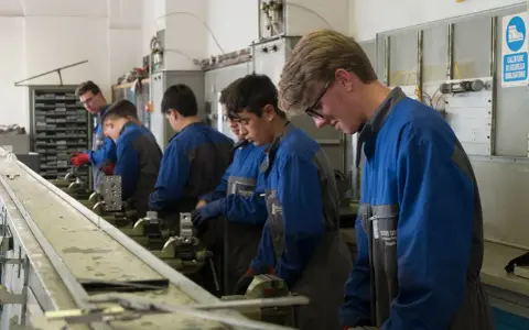 Giovani apprendisti in officina, concentrati sul loro lavoro. L'operatore meccanico cosa fa? Impara a usare strumenti e macchinari per creare e riparare componenti.