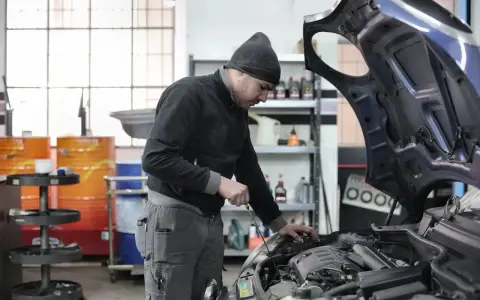 Giovane apprendista meccanico al lavoro, mentre controlla il motore di un'auto. Chissà quanto guadagna un apprendista meccanico con questa dedizione.