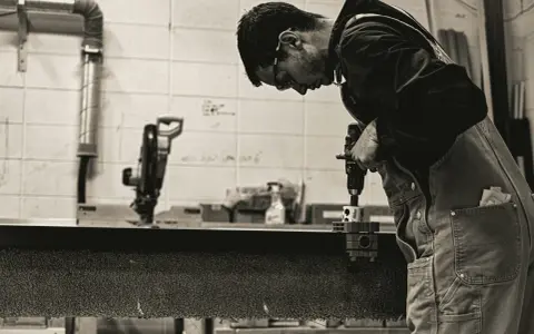 Giovane operatore CNC senza esperienza impara a usare un trapano, concentrato sul lavoro.