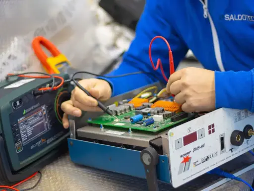 Tecnico effettua la riparazione di saldatrici, testando un circuito elettronico con strumenti di precisione.