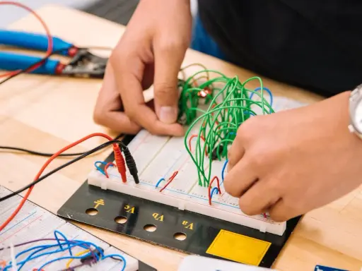 Mani che assemblano circuiti su breadboard, un'attività che fa riflettere su quanto guadagna un meccanico industriale.