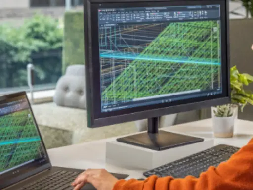 Un inventore lavora su un progetto complesso con AutoCAD, visualizzando modelli 3D su un monitor e un laptop.