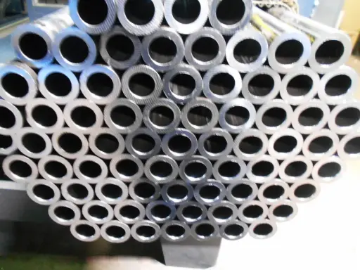 Un mucchio di tubi in acciaio al carbonio, con la sigla visibile su alcuni di essi, pronti per essere utilizzati.