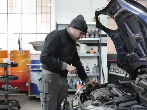 Giovane apprendista meccanico al lavoro, mentre controlla il motore di un'auto. Chissà quanto guadagna un apprendista meccanico con questa dedizione.