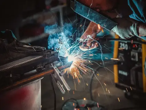 Un operaio con maschera e guanti esegue una saldatura, creando scintille luminose. Il significato della saldatura è unire metalli.