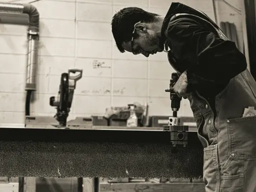Giovane operatore CNC senza esperienza impara a usare un trapano, concentrato sul lavoro.