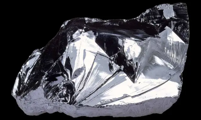 Frammento lucido di silicio puro, metallico, con sfaccettature che riflettono la luce. Il suo elevato punto di fusione lo rende fondamentale nell'elettronica.