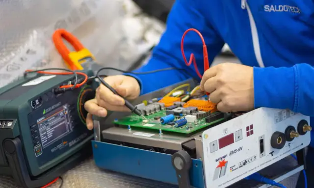 Tecnico effettua la riparazione di saldatrici, testando un circuito elettronico con strumenti di precisione.
