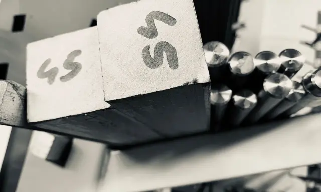Blocchi di metallo con numeri "45" e "55" scritti sopra, pronti per essere lavorati. Accanto, barre di acciaio inossidabile aisi 309 lucide.
