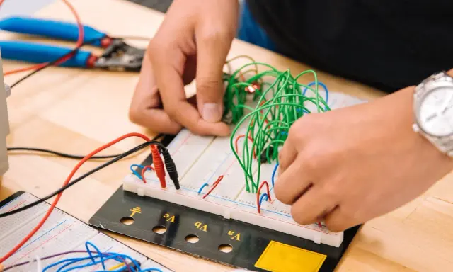Mani che assemblano circuiti su breadboard, un'attività che fa riflettere su quanto guadagna un meccanico industriale.