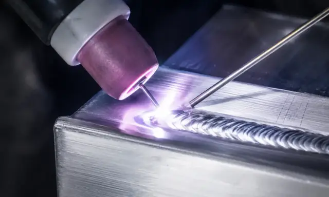 Saldatura magnesio con torcia TIG, creando un cordone preciso e luminoso su un pezzo metallico.