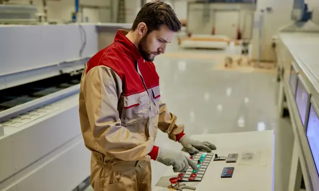 Un tornitore CNC esperto opera un pannello di controllo in una moderna officina, concentrato sul suo lavoro.